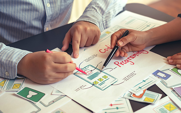 Duas pessoas analisam UX eUI deum aplicativo desenahdo em uma folha de papel.
