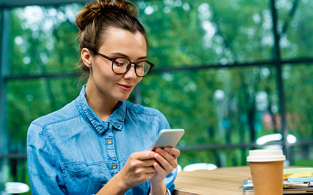 Mulher branca, de óculos, mexendo no celular com uma expressão de satisfação